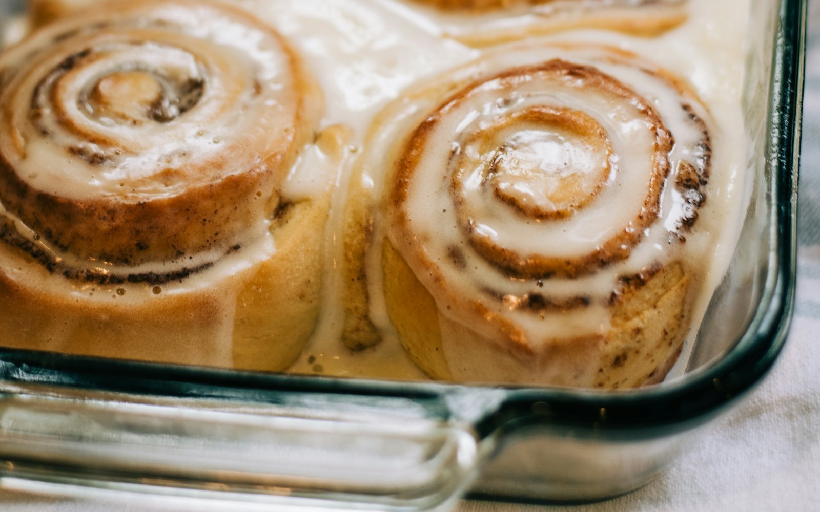 A glass pan of soft cinnamon rolls covered in thick, melting frosting